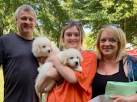 three people holding puppies in a park