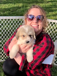 a woman holding a puppy in front of a fence