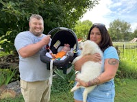 a man and woman holding a baby in a car seat