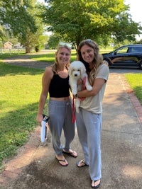 two women standing on a sidewalk with a white dog