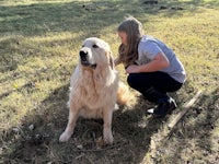a girl kneeling down next to a large golden retriever